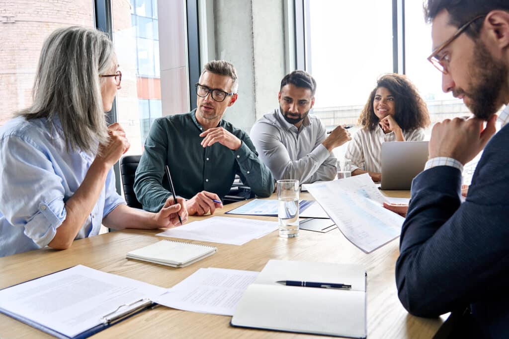 Diverse international executive business partners group discuss report at boardroom meeting table. Multiracial team negotiating project developing business strategy doing paperwork analysis in office.